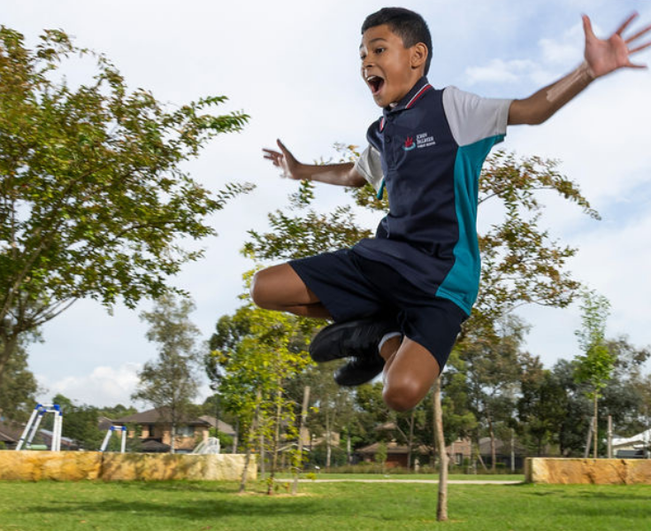 A boy leaping into the air with his arms outstretched and knees up to the side