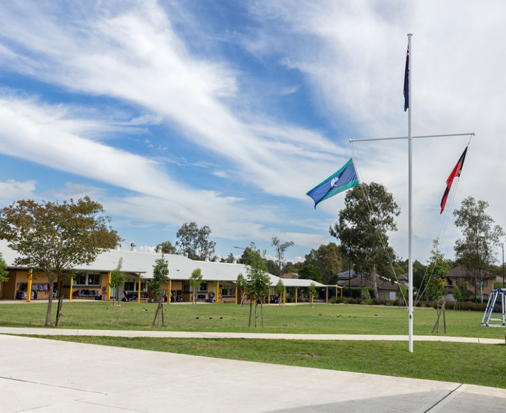 A view of the primary grass area with classrooms visible in the background, and a flagpole to the right of the foreground.