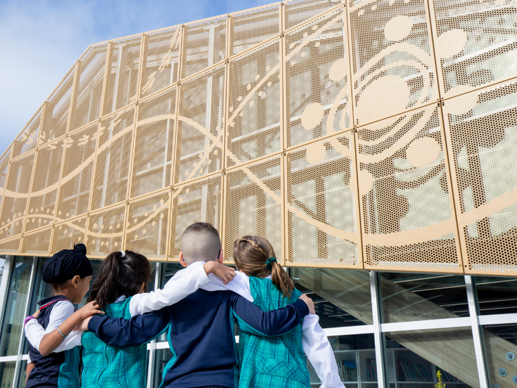 Four students standing arm in arm facing the library.