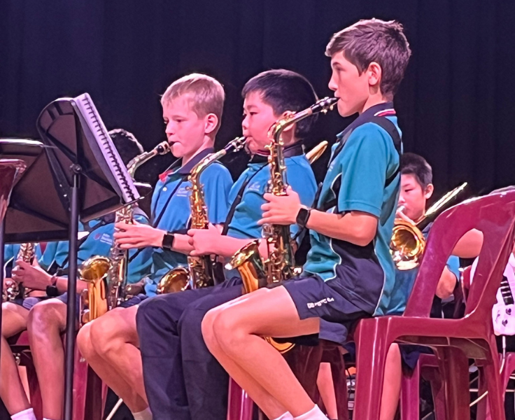 Three students playing saxophone in their sports uniform