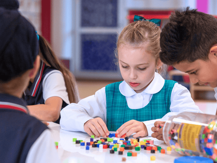 Students at a table using centicubes - only one girl is fully visible, carefully counting the cubes.