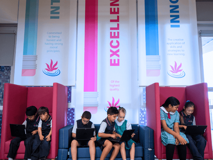 Seven students seated in flexible seating underneath banners bearing the school logo of Integrity, Excellence and Innovation