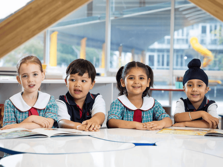 Four students are seated at a table, side by side. There are two girls and two boys.