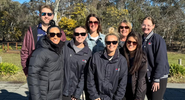 Eight school teachers are posing for a photograph in camping gear