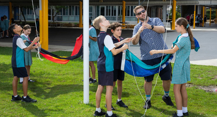 Six school leaders and a teacher raise the Aboriginal and Torres Strait Island flags