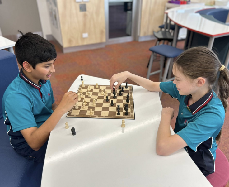 A boy (left) and a girl (right) playing chess in the lilbrary