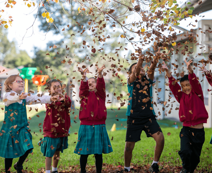 Five students throwing autumn leaves into the air